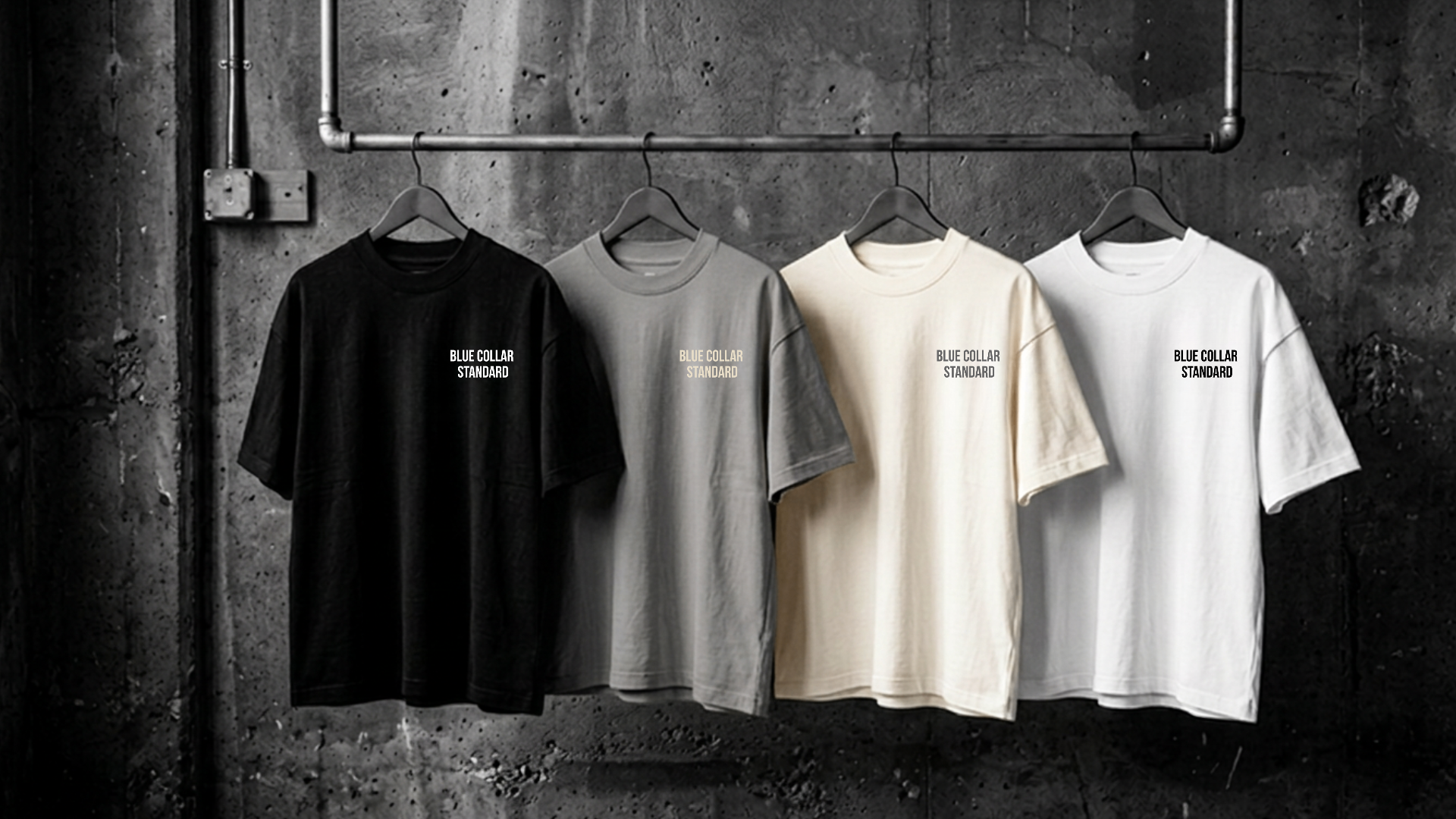 Blue Collar Standard tees hanging on an industrial pipe rack against a concrete wall
